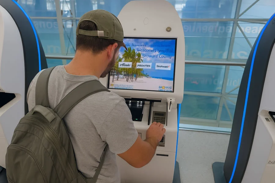 Passenger using self check-in kiosk at Fort Lauderdale Airport with tropical welcome screen